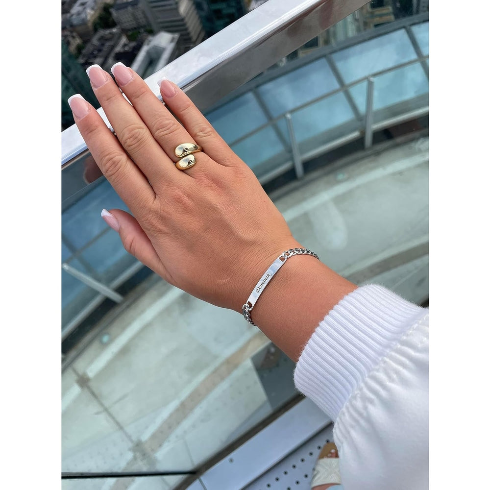 Hand in Hand: Männer- und Frauenhand mit personalisierten Partnerarmbändern, Skyline als Hintergrund.