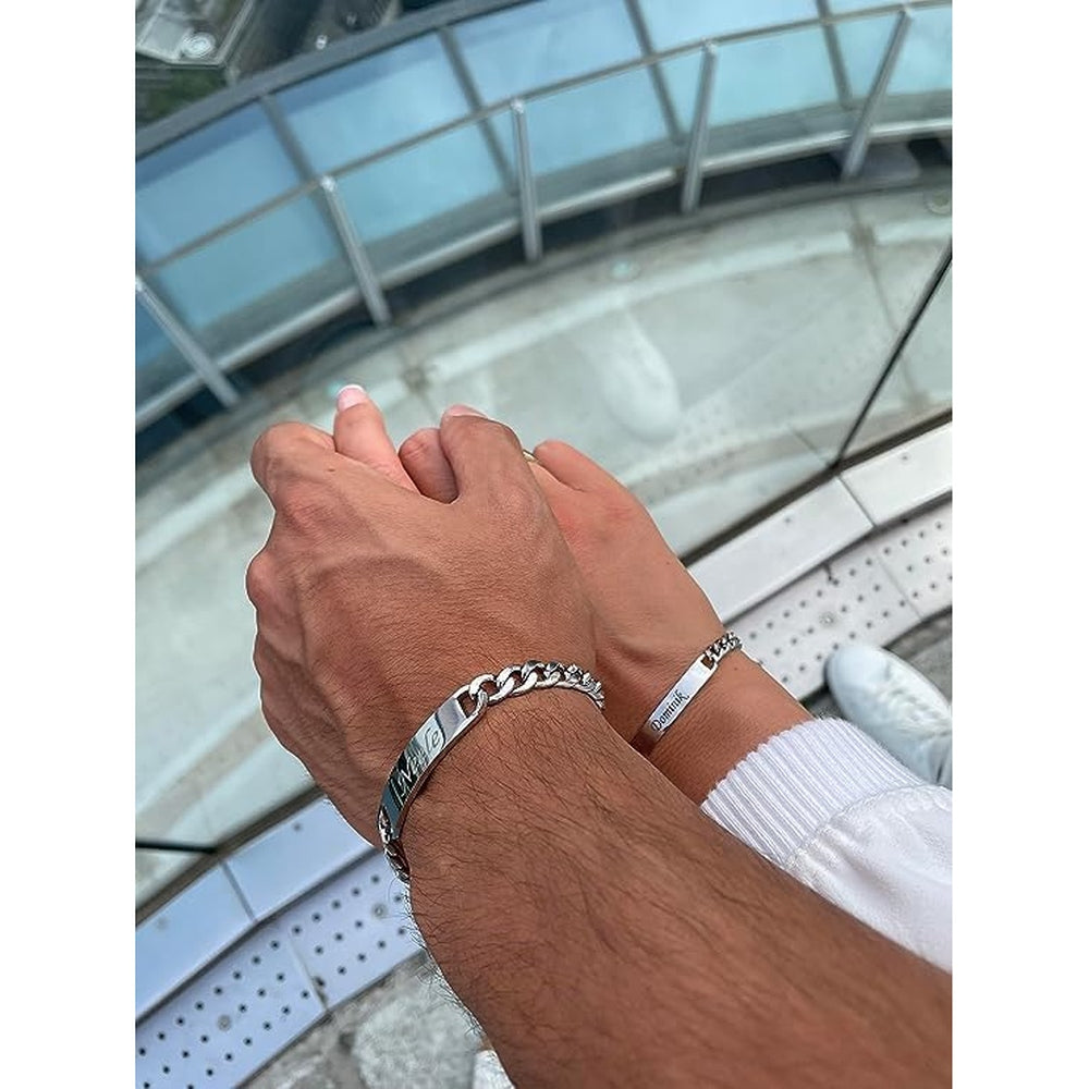 Paar mit Partnerarmbändern: Männer- und Frauenhand tragen Armbänder mit dem Namen des Partners, Skyline im Hintergrund.