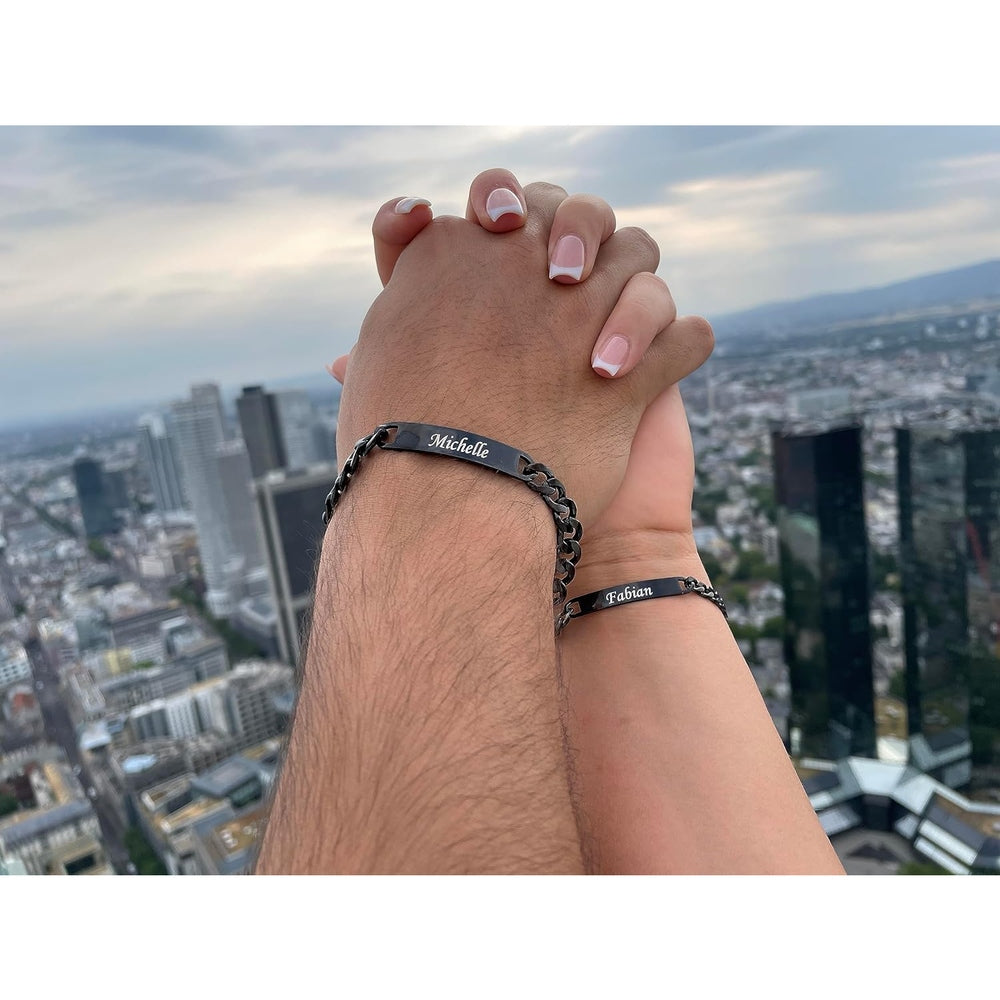 Männer- und Frauenhände mit personalisierten Partnerarmbändern, die Namen des Partners tragen, vor einer Skyline im Hintergrund.